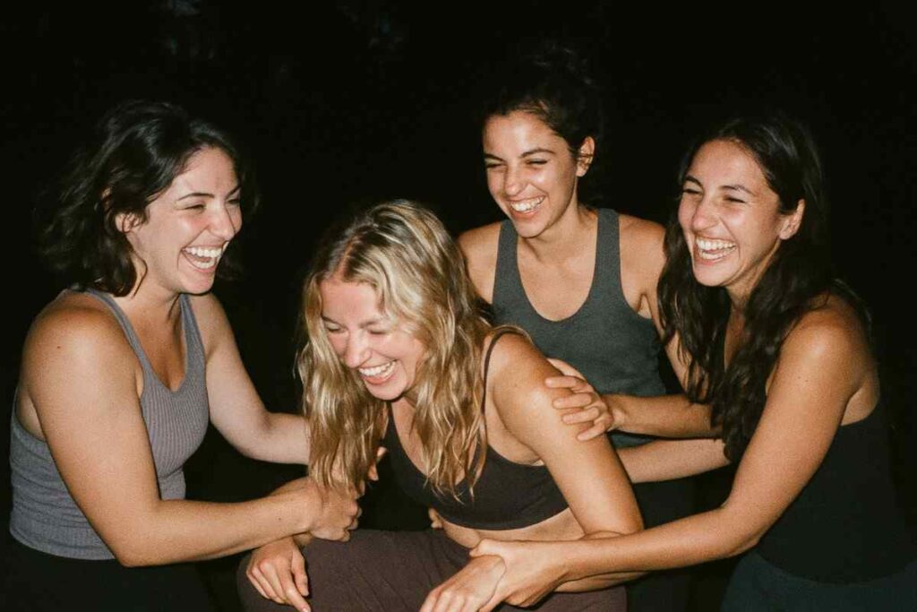 Old digital camera photo with flash at a nighttime group gathering, yoga trainees laughing or supporting each other, blurred motion, high contrast flash lighting, realistic grain, nostalgic softness, close-knit vibe captured imperfectly like a memory
