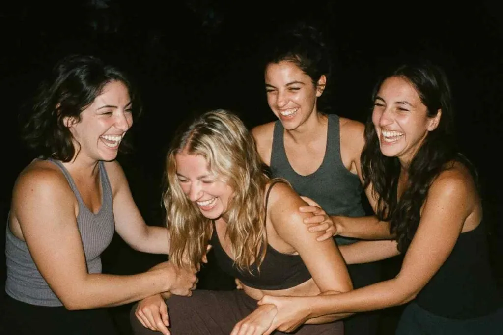Old digital camera photo with flash at a nighttime group gathering, yoga trainees laughing or supporting each other, blurred motion, high contrast flash lighting, realistic grain, nostalgic softness, close-knit vibe captured imperfectly like a memory